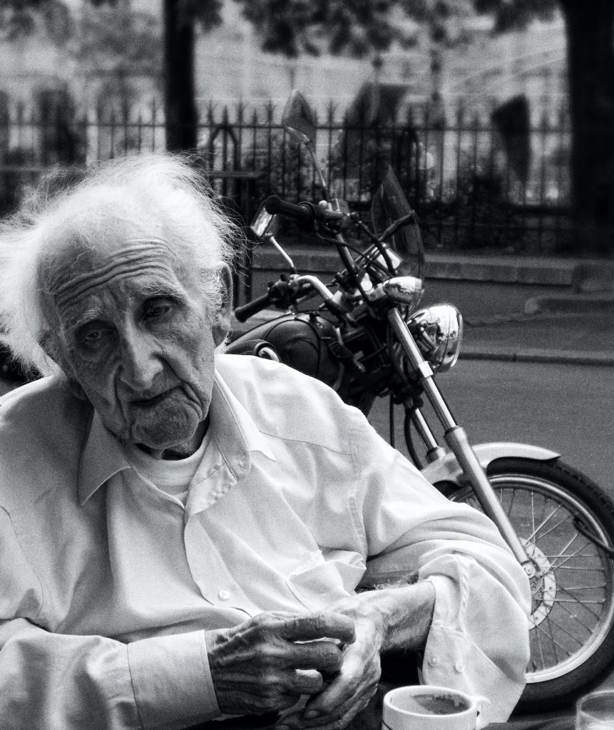 Old man sitting sadly near a motorcycle